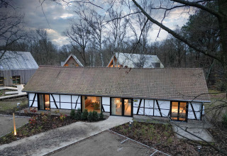Villa Lodge mit Jacuzzi im Woodz Lodges Belgien, umgeben von Wald und modernen Gebäuden in winterlicher Umgebung.