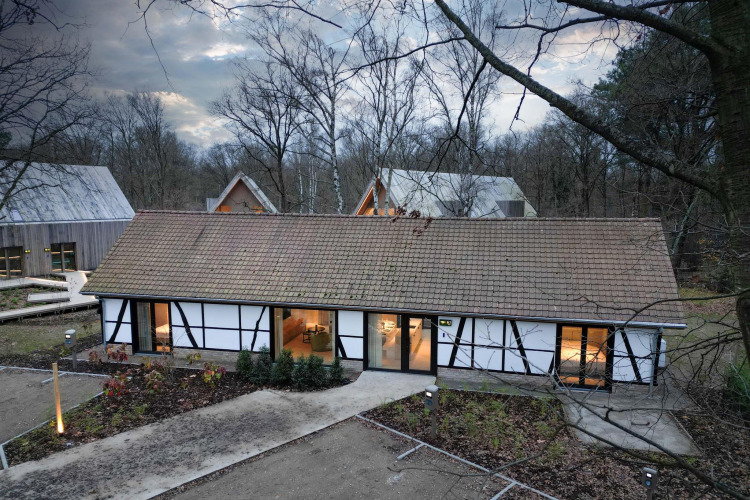 Villa Lodge mit Jacuzzi im Woodz Lodges Belgien, umgeben von Wald und modernen Gebäuden in winterlicher Umgebung.