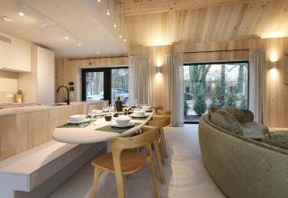 Essbereich und offene Küche in der Villa Lodge mit Whirlpool, Woodz Lodges, Belgien, mit Blick nach außen.