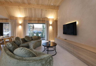 Modernes Wohnzimmer in der Villa Lodge mit geschwungenem Sofa und Flachbild-TV bei Woodz Lodges, Belgien.