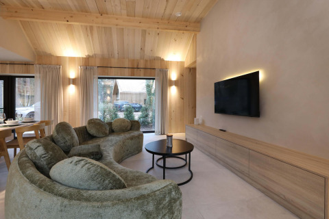 Modernes Wohnzimmer in der Villa Lodge mit geschwungenem Sofa und Flachbild-TV bei Woodz Lodges, Belgien.