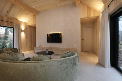 Salon moderne à la Villa Lodge avec jacuzzi aux Woodz Lodges en Belgique, avec canapé rond et bois clair.