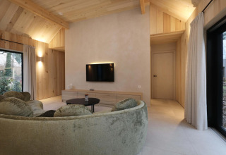 Modern salon in Villa Lodge met jacuzzi bij Woodz Lodges in België, met ronde sofa en veel hout.