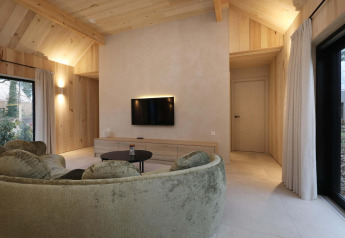 Modern salon in Villa Lodge met jacuzzi bij Woodz Lodges in België, met ronde sofa en veel hout.
