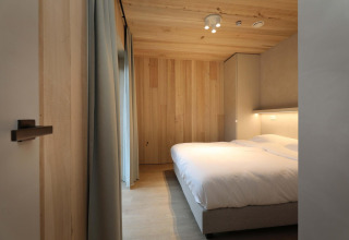 Schlafzimmer der Villa Lodge mit Jacuzzi in den Woodz Lodges, Belgien, mit Holzdesign und Doppelbett.