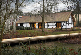 Villa Lodge mit Whirlpool bei Woodz Lodges in Belgien, umgeben von Wald und einem Holzsteg im Vordergrund.