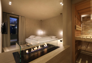 Wellness Suite at Woodz Lodges in Belgium featuring a modern fireplace, cozy bed, and private sauna.