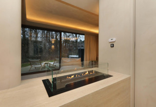 Chimenea moderna en la Wellness Suite de Woodz Lodges, Bélgica, con vistas al jardín y terraza a través de ventanales.