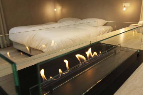 Suite moderna con letto matrimoniale e camino in vetro nel Wellness Suite di Woodz Lodges, Belgio.