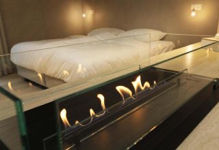 Suite moderna con letto matrimoniale e camino in vetro nel Wellness Suite di Woodz Lodges, Belgio.