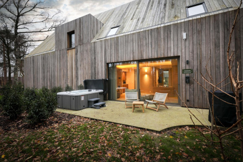Vista exterior de la Wellness Suite en Woodz Lodges, Bélgica, con jacuzzi, sillas de terraza y fachada de madera.