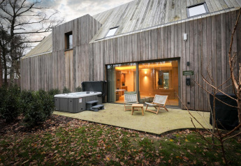 Buitenaanzicht van de Wellness Suite bij Woodz Lodges in België met jacuzzi, terrasstoelen en houten gevel.