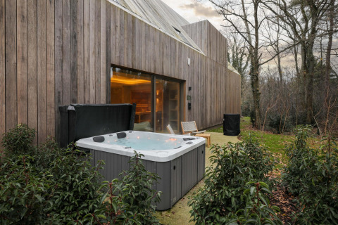 Outdoor hot tub and wooden lodge exterior at Wellness Suite, Woodz Lodges, Belgium, surrounded by trees.
