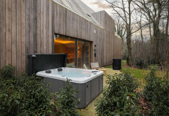 Outdoor hot tub and wooden lodge exterior at Wellness Suite, Woodz Lodges, Belgium, surrounded by trees.