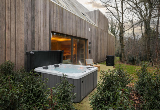 Bain à remous extérieur et lodge moderne à la Wellness Suite de Woodz Lodges, Belgique, entouré d’arbres.