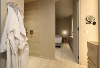 Moderne Wellness Suite bij Woodz Lodges in België met badjassen, slaapkamer en stijlvolle badkamer.