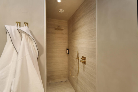 Moderne douche met gouden kranen en badjassen in de Wellness Suite bij Woodz Lodges, België.