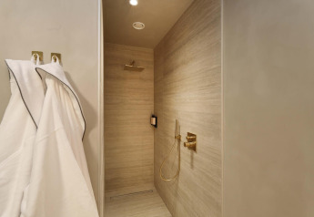 Moderne douche met gouden kranen en badjassen in de Wellness Suite bij Woodz Lodges, België.