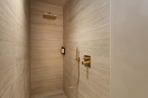 Ducha moderna en la Wellness Suite de Woodz Lodges, Bélgica, con grifería dorada y diseño minimalista.