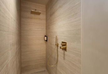 Moderne douche in de Wellness Suite bij Woodz Lodges, België, met goudkleurige kranen en strak design.