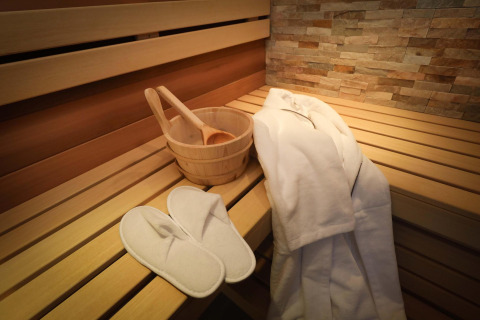 Wooden sauna bench at Wellness Suite, Woodz Lodges, Belgium, with robe, slippers, and ladle bucket.