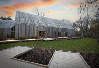 Un albergue moderno de madera con techo inclinado y terrazas, rodeado de césped y árboles al atardecer.