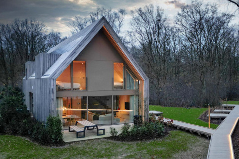 Lodge moderna con grandi finestre e rivestimento in legno immersa in una radura boschiva al tramonto.