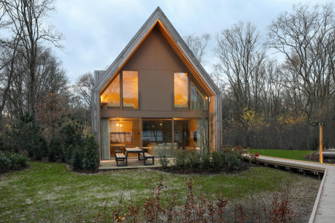 Lodge moderno en Woodz Lodges en Bélgica, con grandes ventanales, mesa exterior y bosque alrededor.