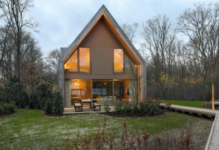 Lodge moderno alle Woodz Lodges in Belgio, ampie finestre, tavolo da esterno e ambiente naturale.