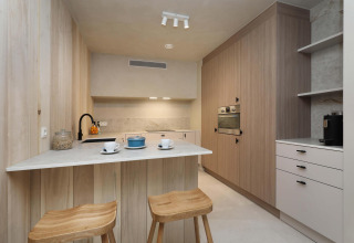 Cocina moderna en Lodge at Woodz Lodges, Bélgica, con paneles de madera, taburetes y diseño minimalista.