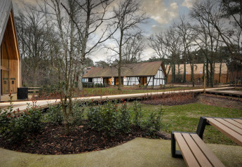 Vista di un lodge ai Woodz Lodges in Belgio, circondato da alberi, piante verdi e panchine moderne.