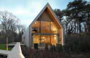 Moderne lodge med store vinduer og varmt lys, omgivet af træer og natur, perfekt til afslapning.