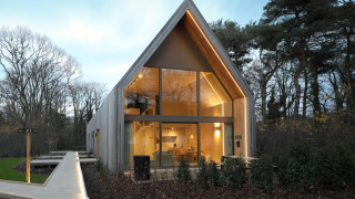 Lodge moderna con ampie finestre e luci accoglienti, immersa tra alberi in un ambiente naturale.