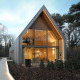 Moderne lodge med store vinduer og varmt lys, omgivet af træer og natur, perfekt til afslapning.