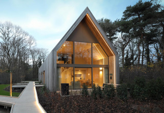 Moderne lodge met hoge ramen en gezellige verlichting, midden in een bosrijke en natuurlijke omgeving.