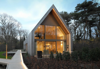 Lodge moderna con grandes ventanales y cálida iluminación, rodeada de árboles y naturaleza pintoresca.