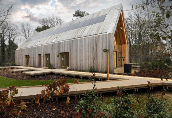 Un lodge moderno de madera con paneles solares en el techo, rodeado de pasarela de madera y árboles.