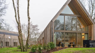 Außenansicht der Lodge mit Jacuzzi, modernes Holzhaus mit großen Fenstern in bewaldeter Umgebung.