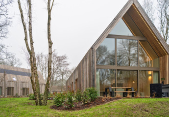 Buitenaanzicht van de Lodge met Jacuzzi, moderne houten gevel met grote ramen in een bosrijk gebied.