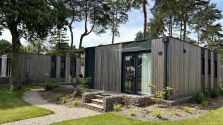 Modernes Chalet Domus 4 mit Holzverkleidung und großen Fenstern, umgeben von Bäumen und Rasenflächen.