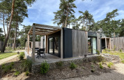 Chalet moderne Domus 4 en bois au Zilverstrand, Belgique, avec terrasse entouré d’arbres verts.