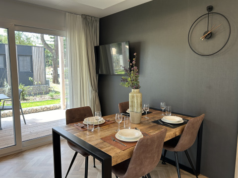 Espace repas moderne dans le chalet Domus 4 au Zilverstrand, Belgique, avec table en bois et horloge murale.