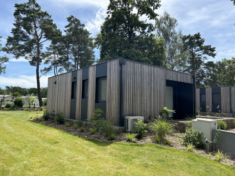 Chalet Domus 4 aan het Zilverstrand in België, modern houten huis omringd door bomen en verzorgde tuin.