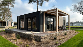 Moderno lodge Belsano 6 con terrazza in legno e pergolato, circondato da verde e alberi alti.
