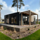 Moderne lodge Belsano 6 med træterrasse og pergola beliggende i grønne omgivelser under høje træer.