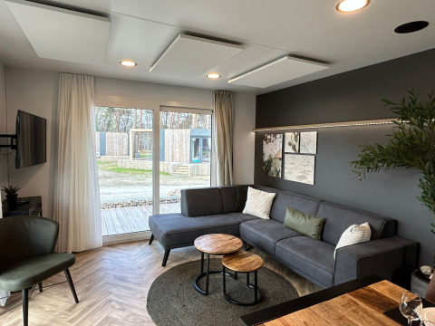 Salon moderne du lodge Belsano 6 au Zilverstrand en Belgique, avec canapé gris et grandes baies vitrées.