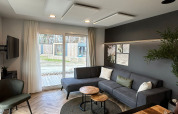 Salon moderne du lodge Belsano 6 au Zilverstrand en Belgique, avec canapé gris et grandes baies vitrées.