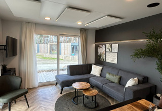 Salon moderne du lodge Belsano 6 au Zilverstrand en Belgique, avec canapé gris et grandes baies vitrées.