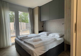 Dormitorio moderno en la cabaña Belsano 6 en Zilverstrand, Bélgica, con cama doble y ventanales amplios.