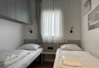 Chambre de lodge moderne avec deux lits simples, fenêtre et décoration minimaliste à Belsano 6 en Belgique.